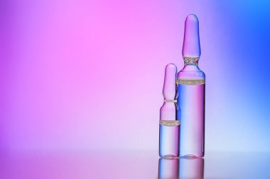 Renkli arka planda temiz sıvı bulunan iki cam tıbbi ampul. İlaç, aşılama, iğne, uyuşturucu konsepti.