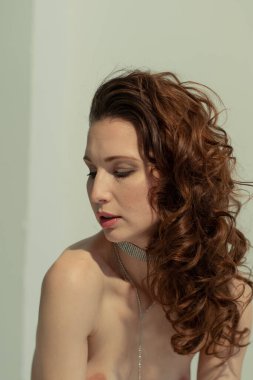 Stüdyoda çıplak poz veren, saçları açık genç bir kadın.