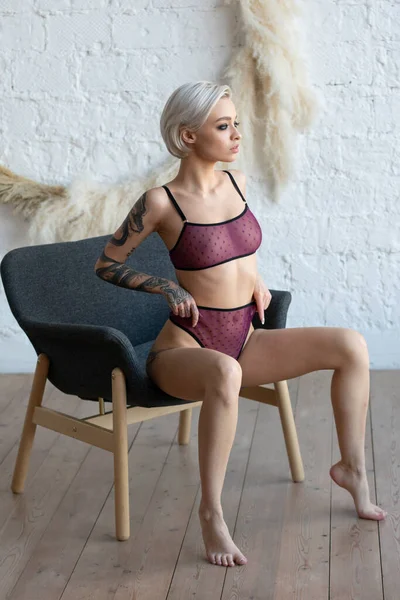 İç çamaşırlarıyla poz veren genç ve güzel bir kadın. Sandalyede oturuyor.