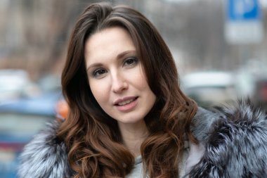 Dışarıda poz veren genç, güzel bir kadın, siyah kürk manto giymiş.