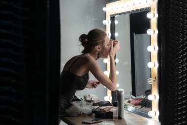 Genç ve güzel bir kız aynanın yanında duruyor, makyaj yapıyor.
