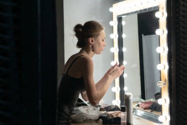 Genç ve güzel bir kız aynanın yanında duruyor, makyaj yapıyor.