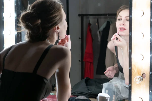young beautiful woman puts on makeup in front of the mirror in a black dress