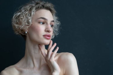 Stüdyoda bir kadının portresi, siyah bir duvarın yanında.