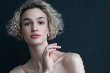 Stüdyoda bir kadının portresi, siyah bir duvarın yanında.