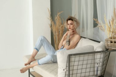 Stüdyoda poz veren genç, güzel bir kadın, mavi kotlu bir sandalyede oturuyor.