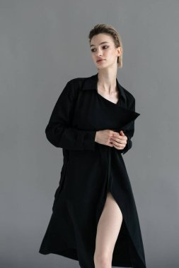 Genç ve güzel bir kadın stüdyoda siyah bir pelerinle poz veriyor.