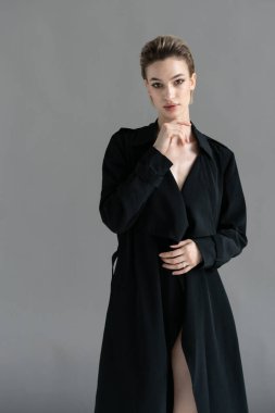 Genç ve güzel bir kadın stüdyoda siyah bir pelerinle poz veriyor.