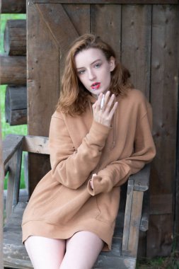 Taşralı kadın elinde sigarayla ahırın yanında oturuyor.