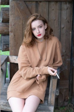 Taşralı kadın elinde sigarayla ahırın yanında oturuyor.