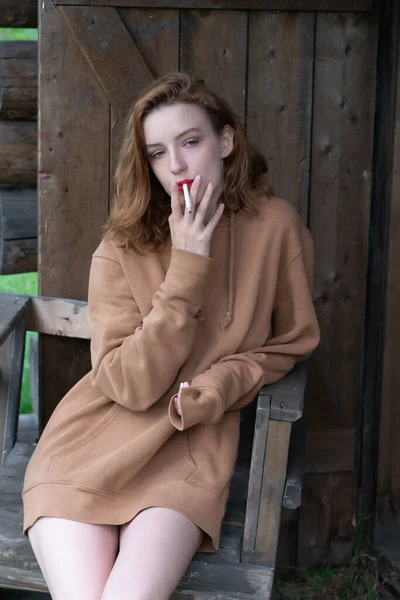 country woman sits near the barn with a cigarette