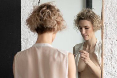 Genç ve güzel bir kadın aynanın yanında dudak boyuyor.