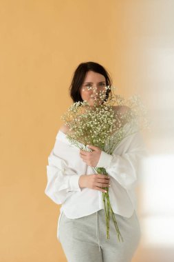 Stüdyoda beyaz çiçeklerle poz veren güzel bir kadın.