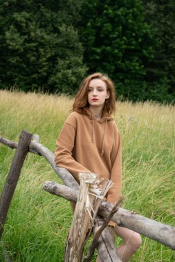 Yazın kahverengi bir kazakla tarlada poz veren güzel bir kadın.