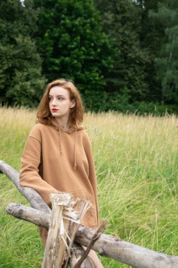 Yazın kahverengi bir kazakla tarlada poz veren güzel bir kadın.