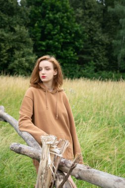 Yazın kahverengi bir kazakla tarlada poz veren güzel bir kadın.