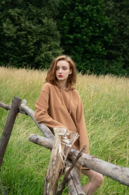 Yazın kahverengi bir kazakla tarlada poz veren güzel bir kadın.