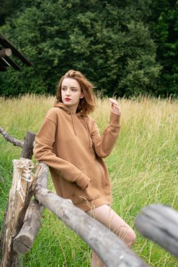 Yazın kahverengi bir kazakla tarlada poz veren güzel bir kadın.