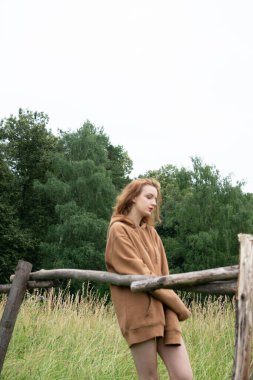 Yazın kahverengi bir kazakla tarlada poz veren güzel bir kadın.