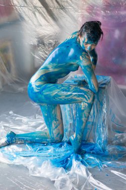 Genç ve güzel bir kadın çıplak poz veriyor, mavi boya ile boyanmış.