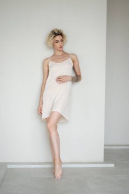 Genç ve güzel bir kadın stüdyoda beyaz bir gecelikle poz veriyor.