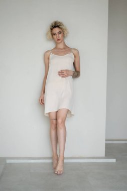 Genç ve güzel bir kadın stüdyoda beyaz bir gecelikle poz veriyor.