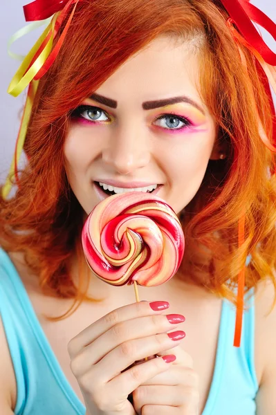 Jovem atraente menina de cabelo vermelho mordendo pirulito colorido — Fotografia de Stock