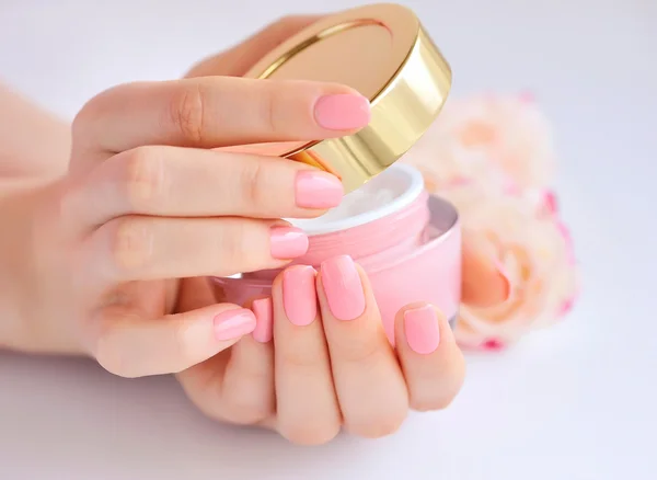 Tangan seorang wanita dengan manikur merah muda dengan krim — Stok Foto