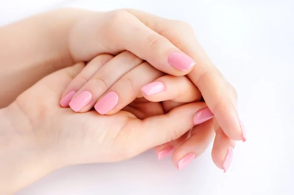 Primer plano de las manos de una joven con manicura rosa en las uñas sobre fondo blanco — Foto de Stock