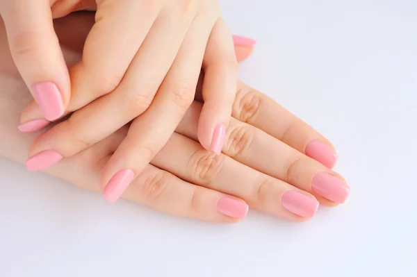 Close-up van handen van een jonge vrouw met roze manicure op nagels tegen witte achtergrond — Stockfoto
