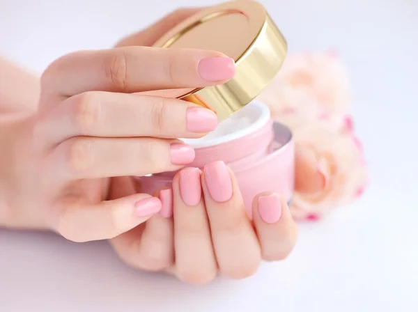 Mãos de uma mulher com manicure rosa com creme — Fotografia de Stock