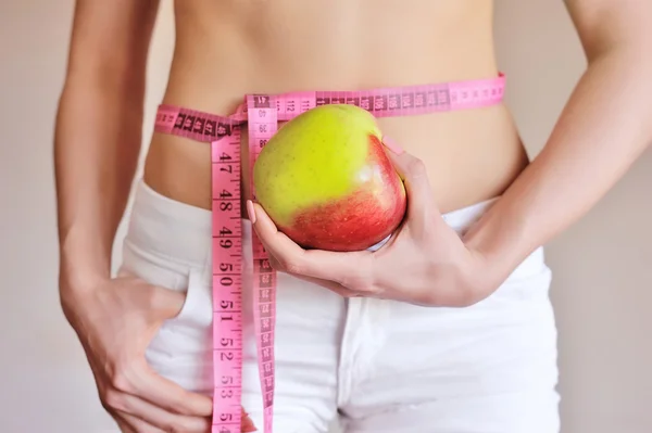 Jonge vrouw is het meten van lichaam en houd appel — Stockfoto