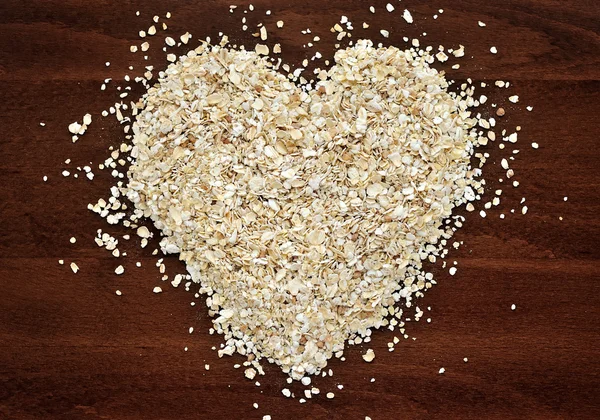 Forma de corazón hecha de copos de avena en mesa de madera oscura — Foto de Stock