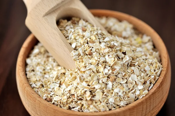 Oatmeal or oat flakes in bowl and scoop on dark wooden table — Stock Photo, Image