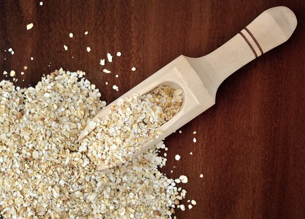 Oat flakes in wooden scoop on wooden background — Stock Photo, Image