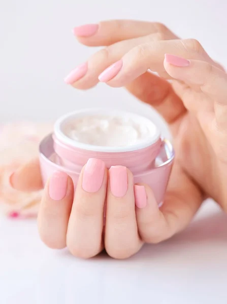 Tangan seorang wanita dengan manikur merah muda dengan krim — Stok Foto
