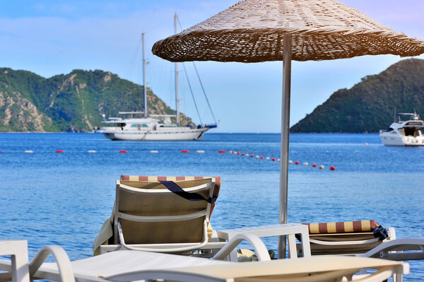 Beach with umbrella and sunbeds against the backdrop of the sea and boats