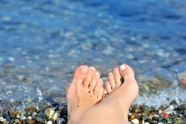 Mädchenbein auf bunten Kieselsteinen am Strand am Meer — Stockfoto