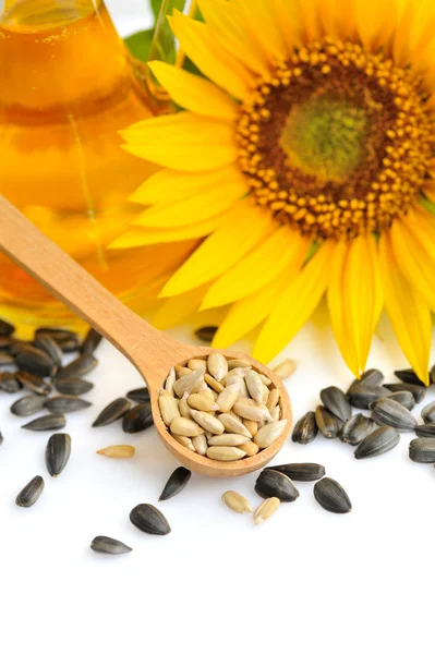 Cucchiaio di legno con semi di girasole su uno sfondo di fiori e una bottiglia di olio — Foto Stock
