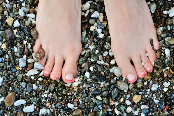 Mädchenbein auf bunten Kieselsteinen am Strand am Meer — Stockfoto