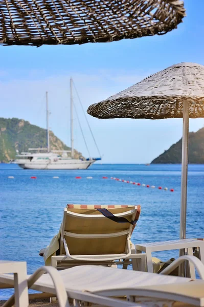 Spiaggia con ombrellone e lettini sullo sfondo del mare e barche — Foto Stock