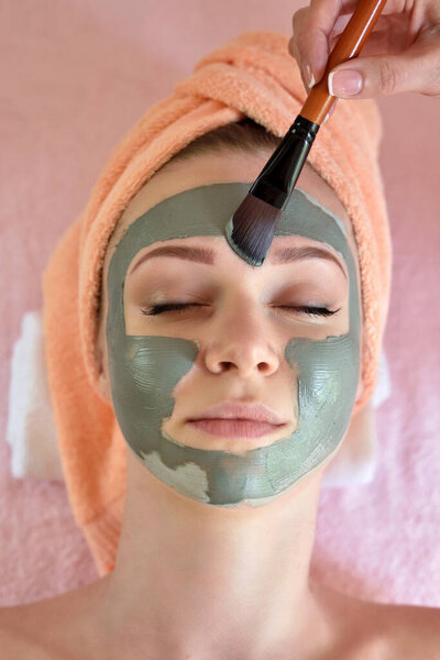 Face peeling mask, spa beauty treatment, skincare. Woman getting facial care by beautician at spa salon, side view, close-up