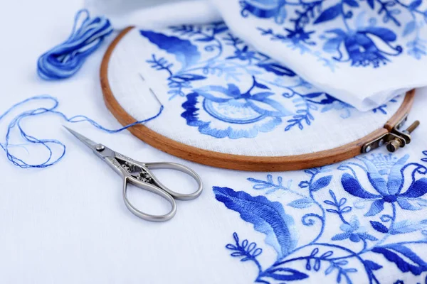 İşlemeli halka kumaş, dikiş iğnesi ve iplik. Beyaz arkaplanda el yapımı mavi çiçek deseni