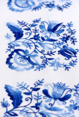 İnce bir tuvale el nakışı dikişleri. Beyaz arka planda mavi çiçek süsü. Sanat ve zanaat kavramı.