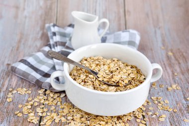 Kırsal masadaki beyaz bir kasede pişmemiş yulaf gevreği. Kahvaltıda sağlıklı yemek.