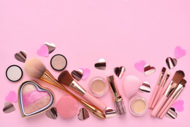 Makyaj fırçaları, dekoratif kozmetikler, pembe arka planda kalpler. Üst görünüm