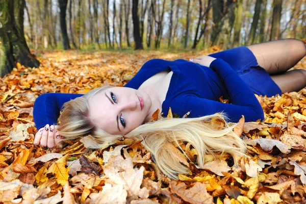 Schöne junge Frau, die in einem Laubhaufen liegt. — Stockfoto