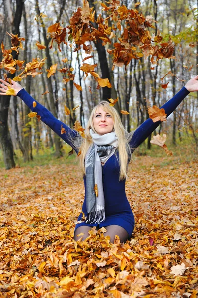 Счастливая женщина, играющая с осенними листьями в лесу — стоковое фото