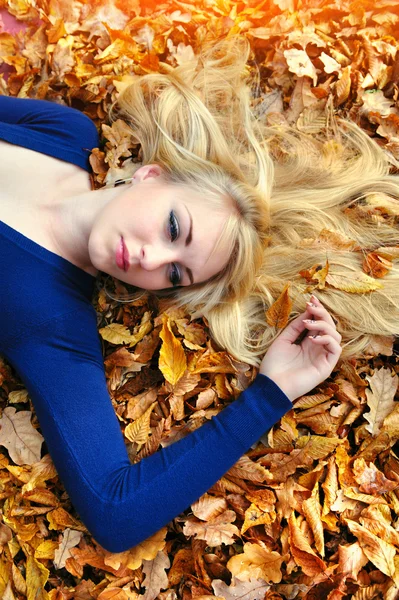 Mooie jonge vrouw liggen in een stapel van bladeren. — Stockfoto