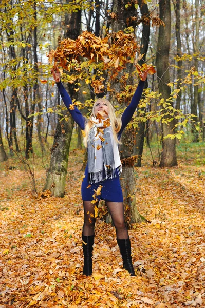 Счастливая женщина, играющая с осенними листьями в лесу — стоковое фото
